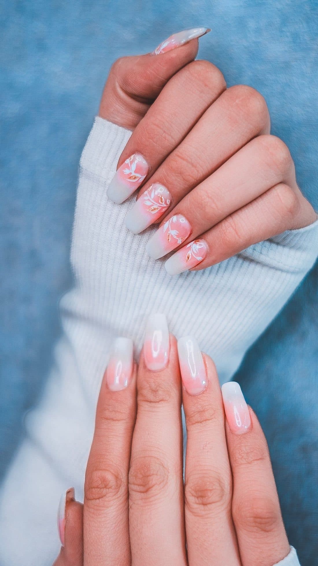 Uñas con degradado y diseño floral sobre un suéter blanco
